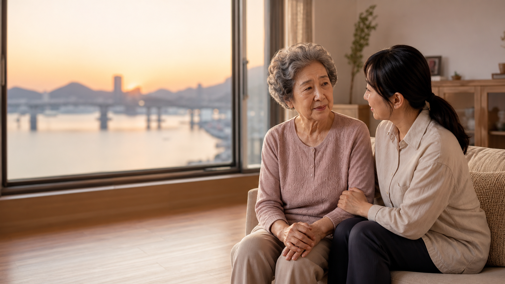 부산의 따뜻한 노을이 보이는 집에서 어르신과 돌봄 인력이 대화를 나누는 모습